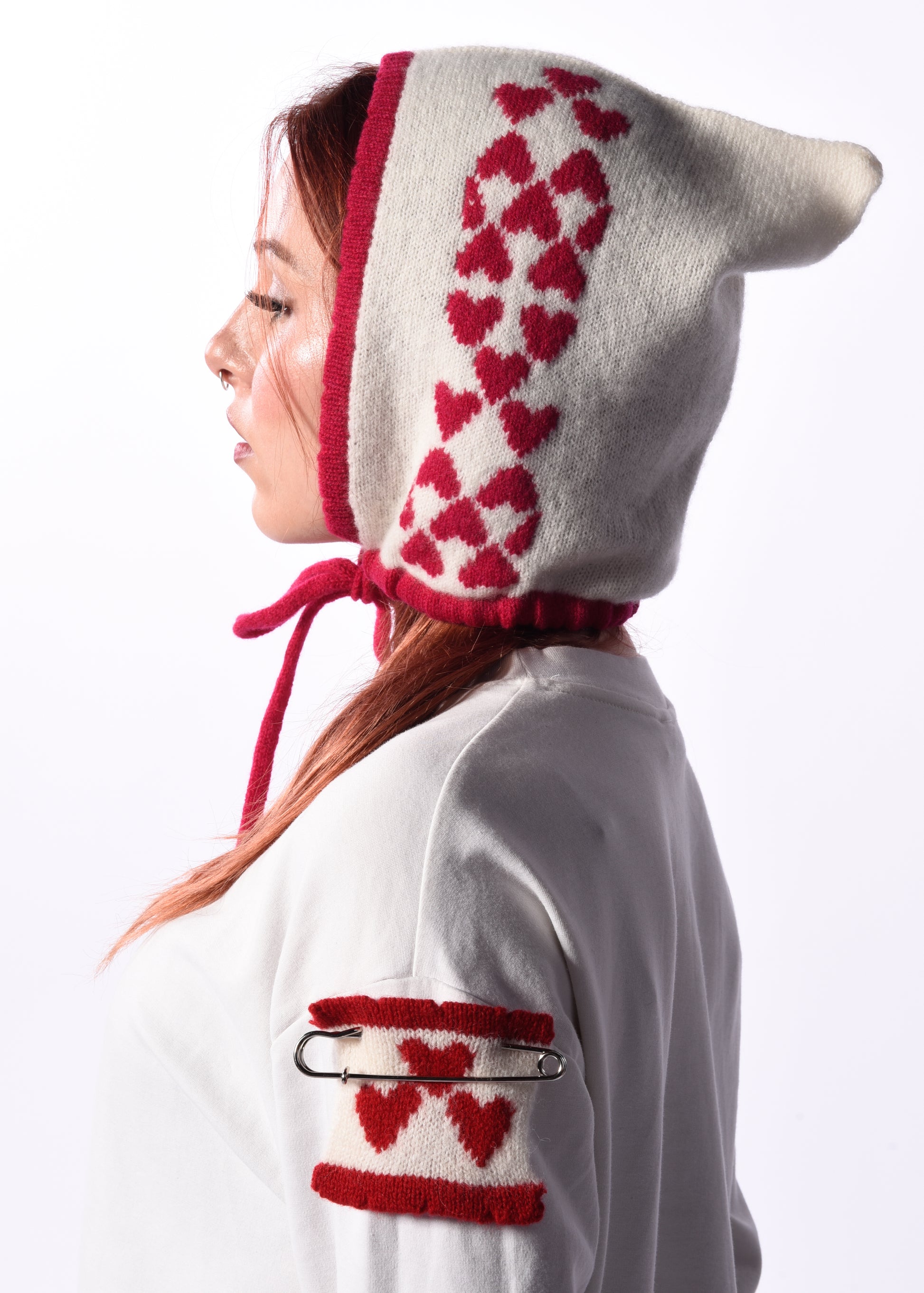 Person wearing a white hood with pink heart patterns on a plain background