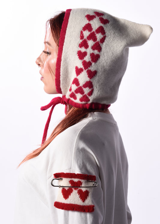 Person wearing a white hood with pink heart patterns on a plain background