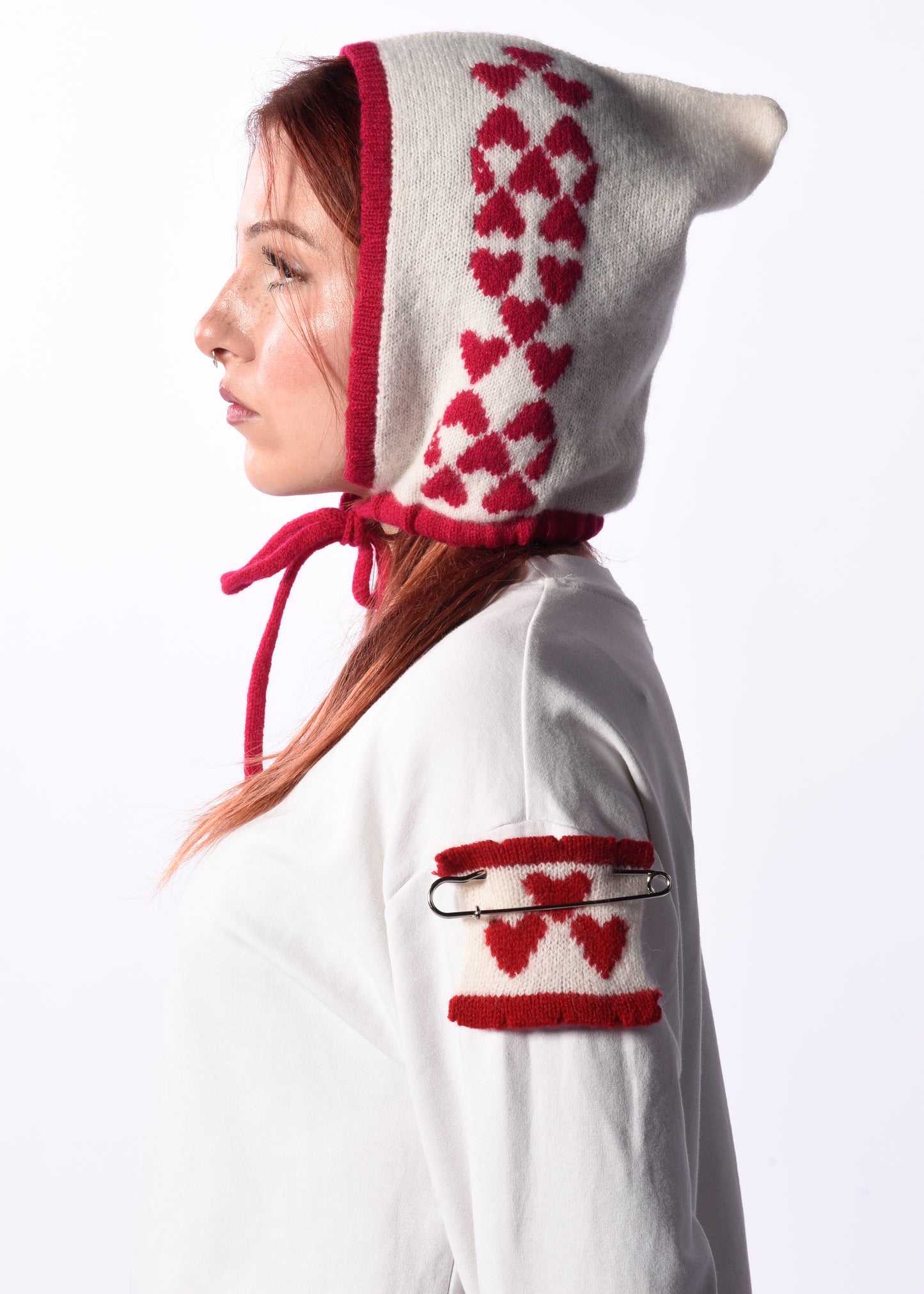 Person wearing a white hooded garment with pink heart patterns on a plain background