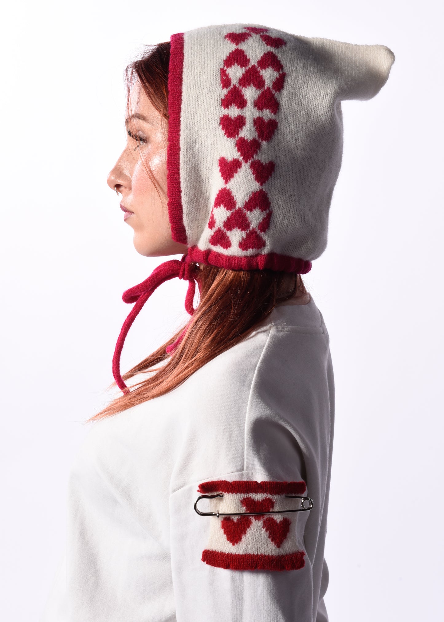 Person wearing a white knitted bonnet with pink heart patterns on a white background