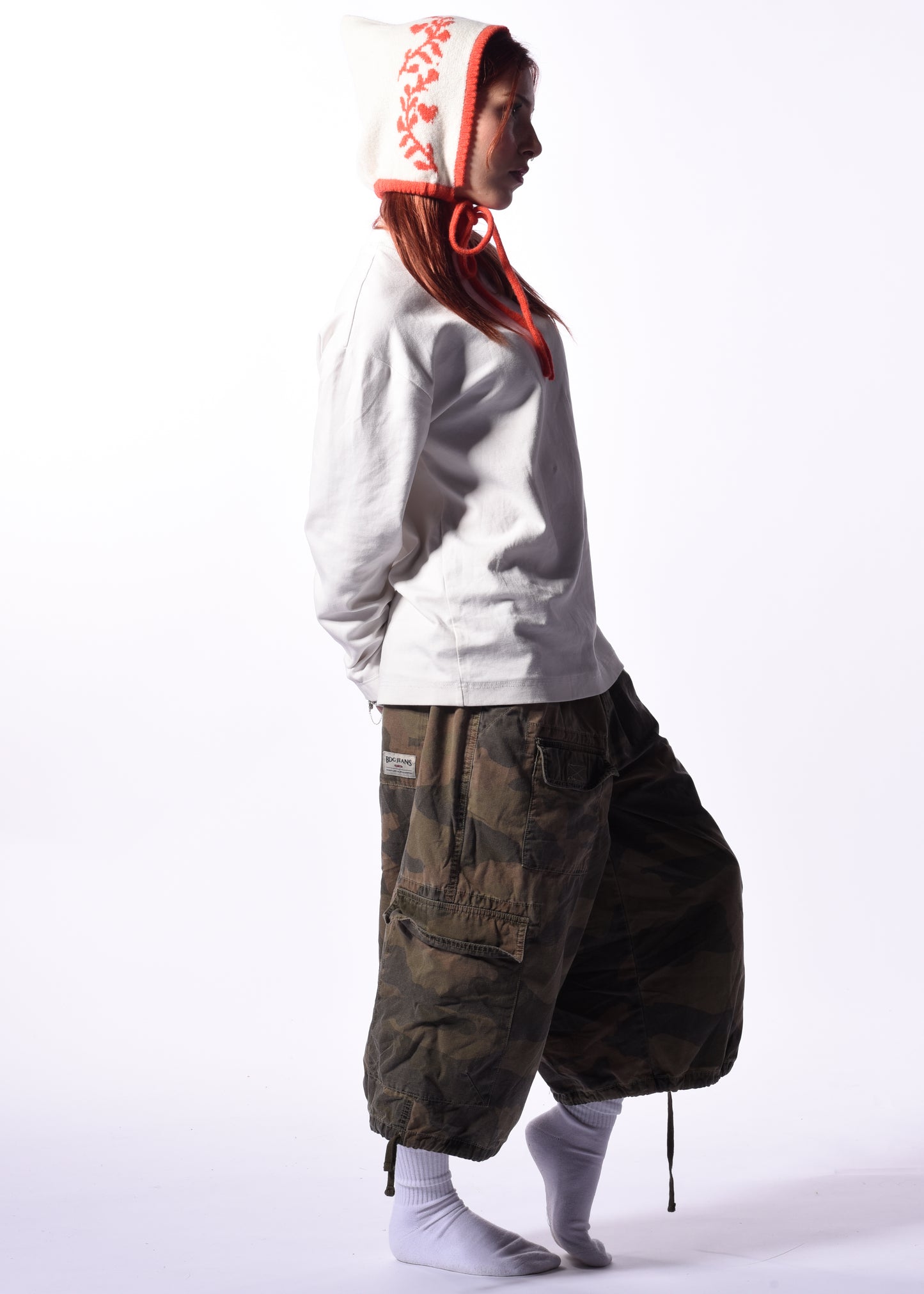 Person wearing a white hoodie with a orange hood design and dark cargo pants on a white background
