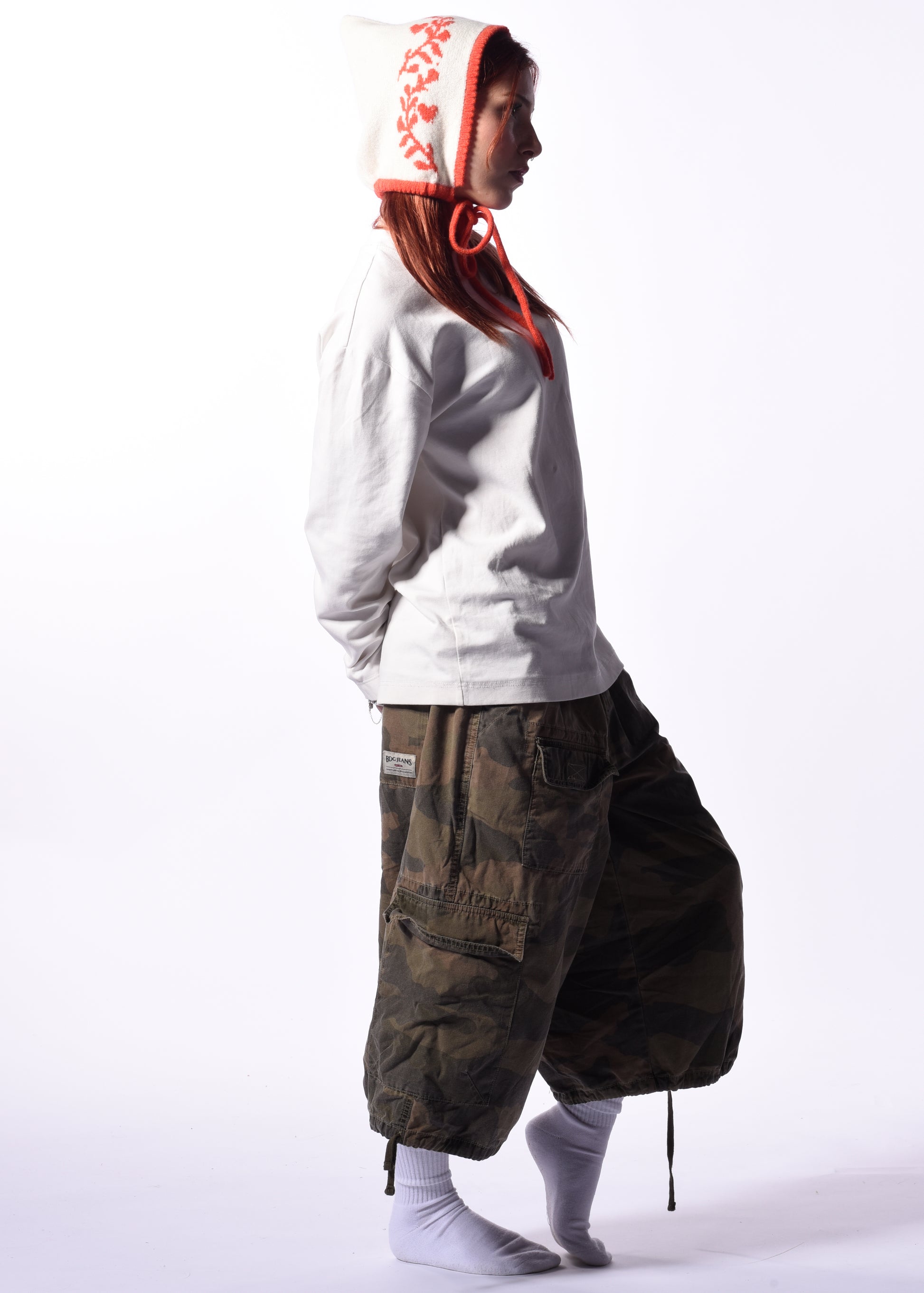 Person wearing a white hoodie with a orange hood design and dark cargo pants on a white background