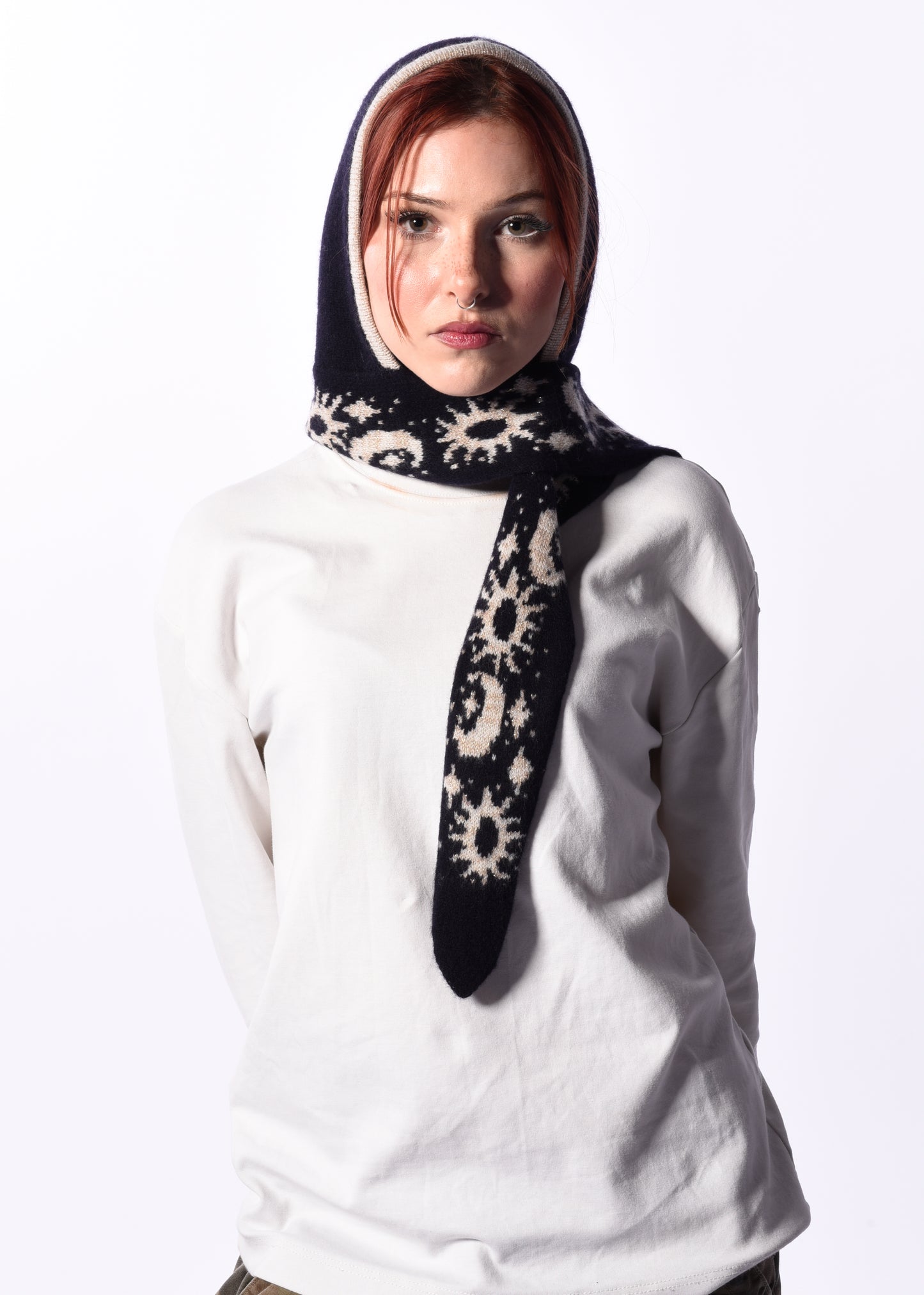 Woman wearing a white top and a patterned hooded scarf bonnet on a white background