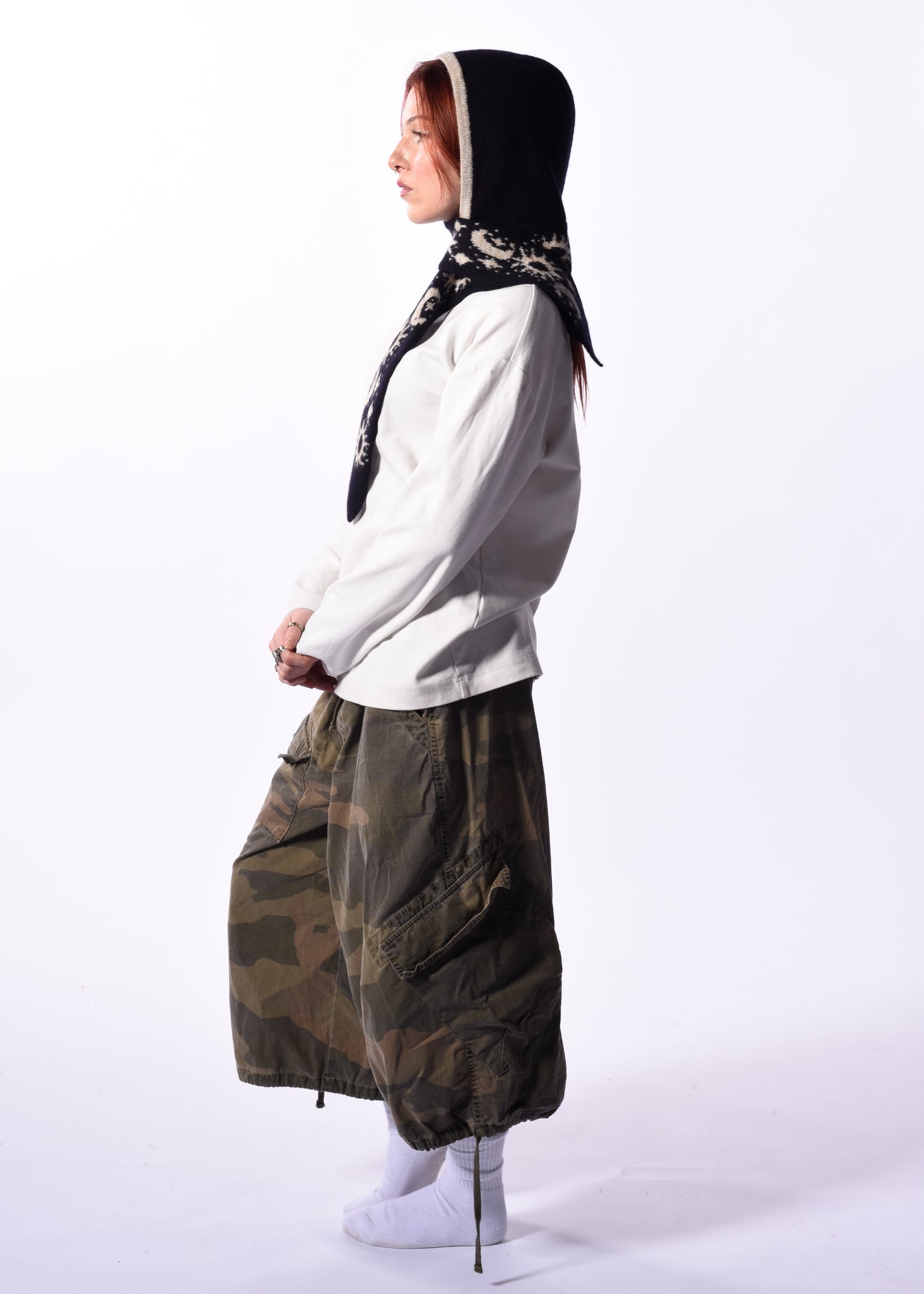 Person wearing a white hoodie and camouflage pants with a black scarf bonnet on a white background