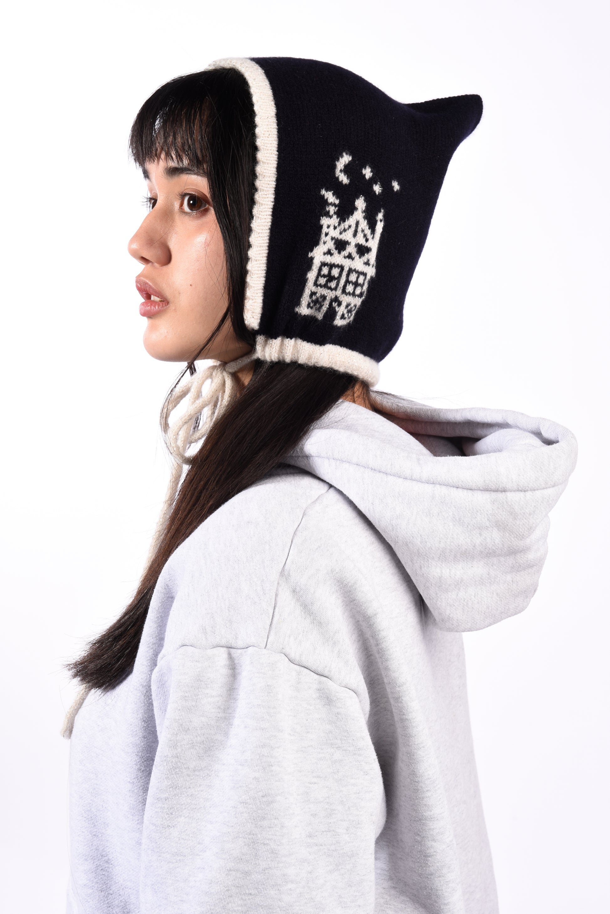 Person wearing a navy and white knitted bonnet with a design, paired with a light gray hoodie on a white background.