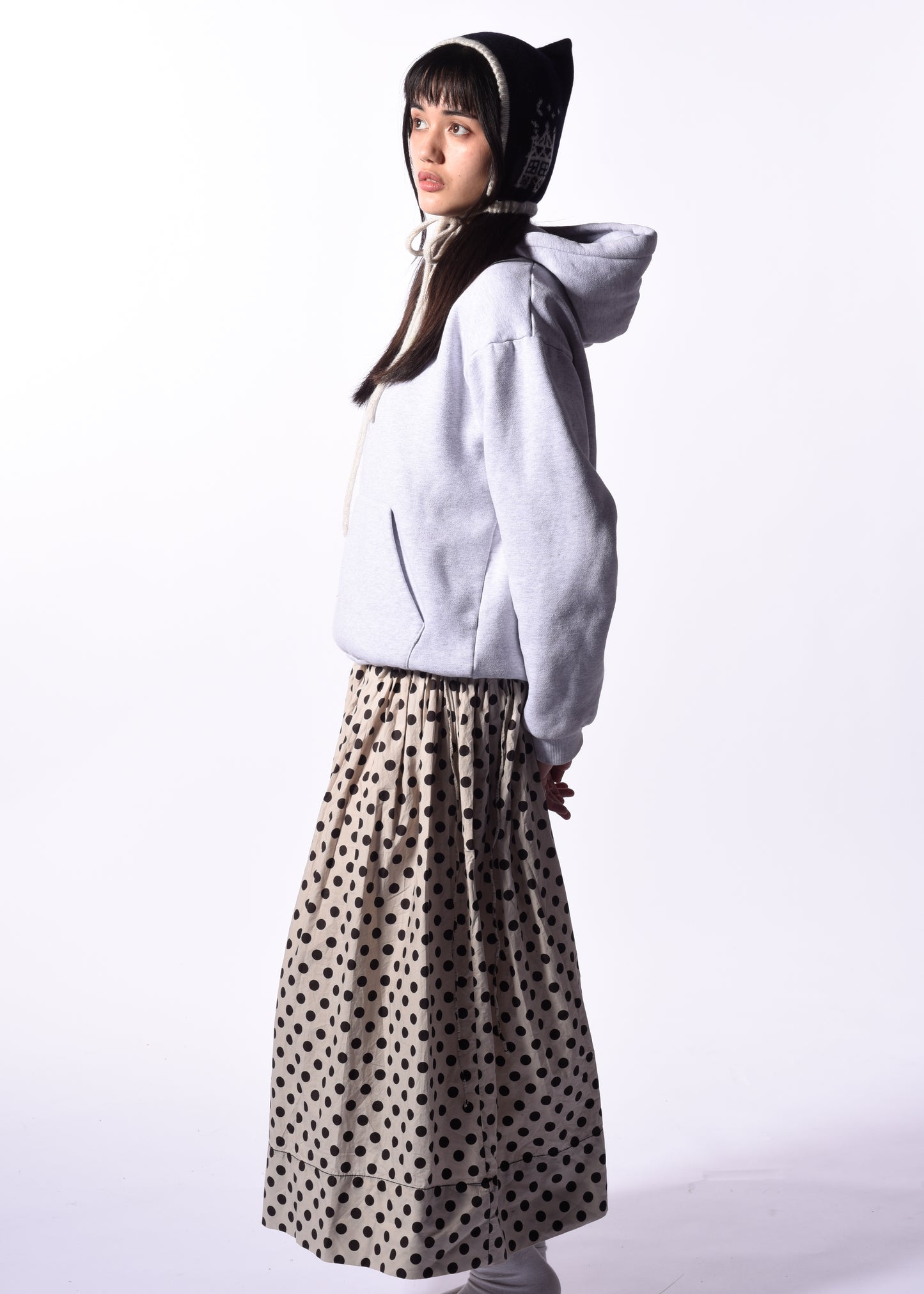 Person wearing a white hoodie and polka dot skirt on a white background