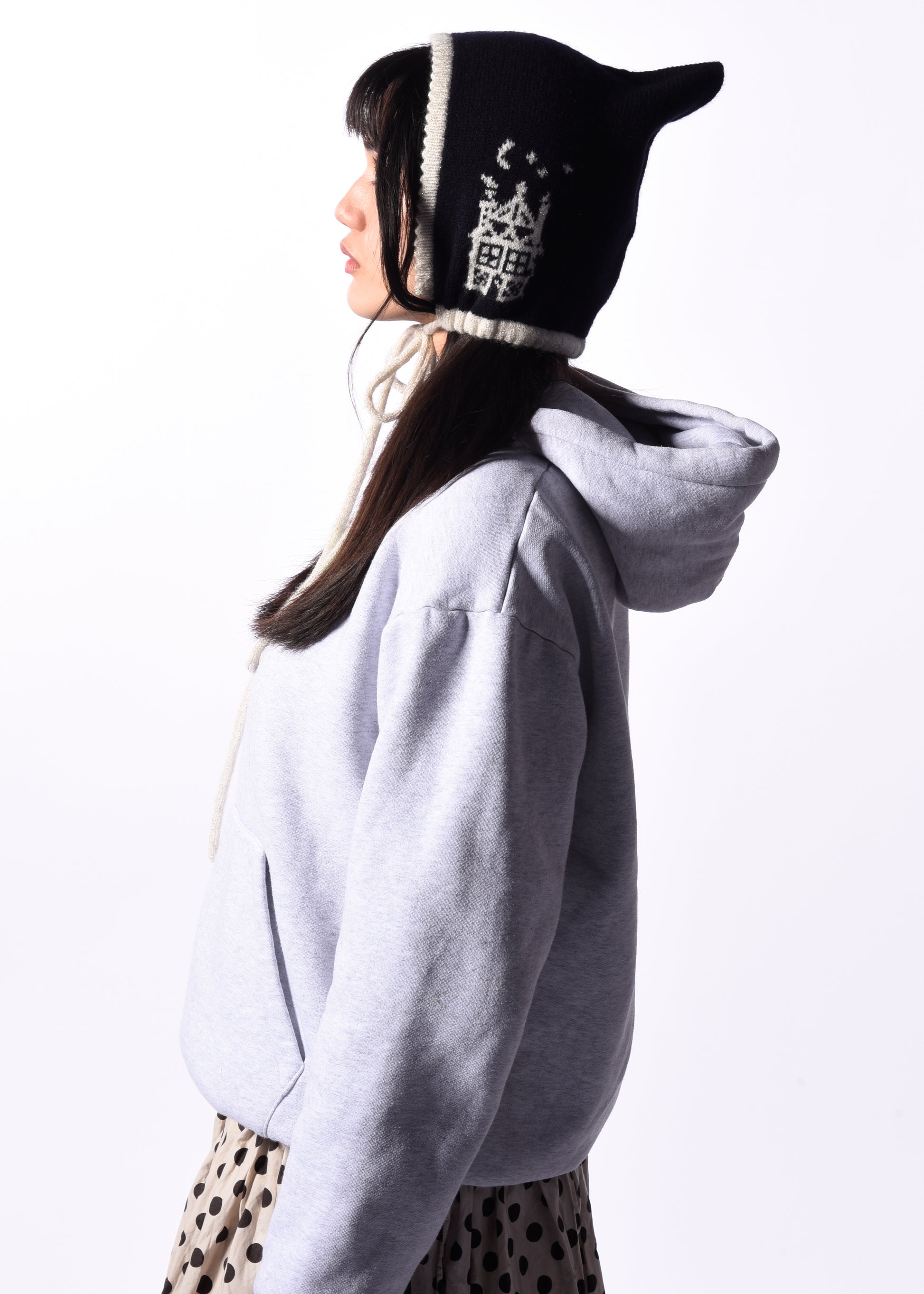 Person wearing a light gray hoodie and a navy bonnet with white patterns on a white background