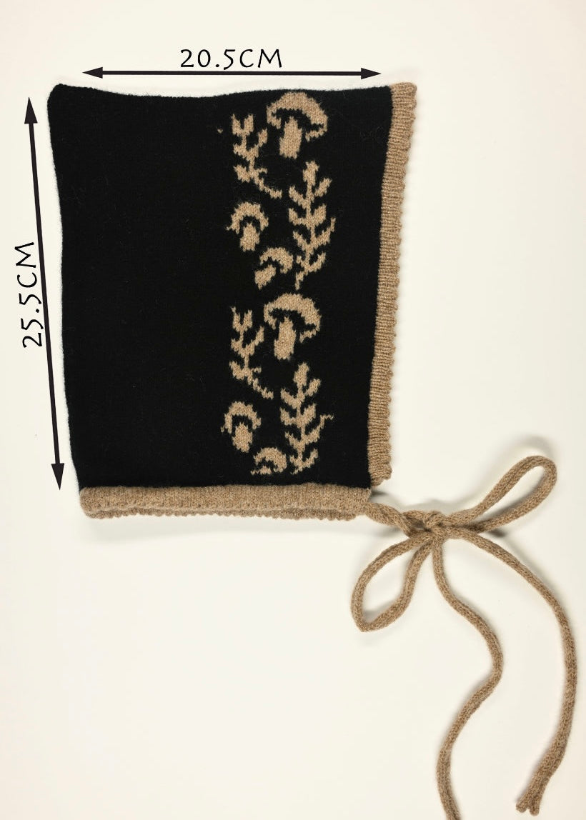 Black knitted bonnet with beige mushroom pattern and drawstring, shown with measurements of 20.5cm wide by 25.5cm long on a white background. 