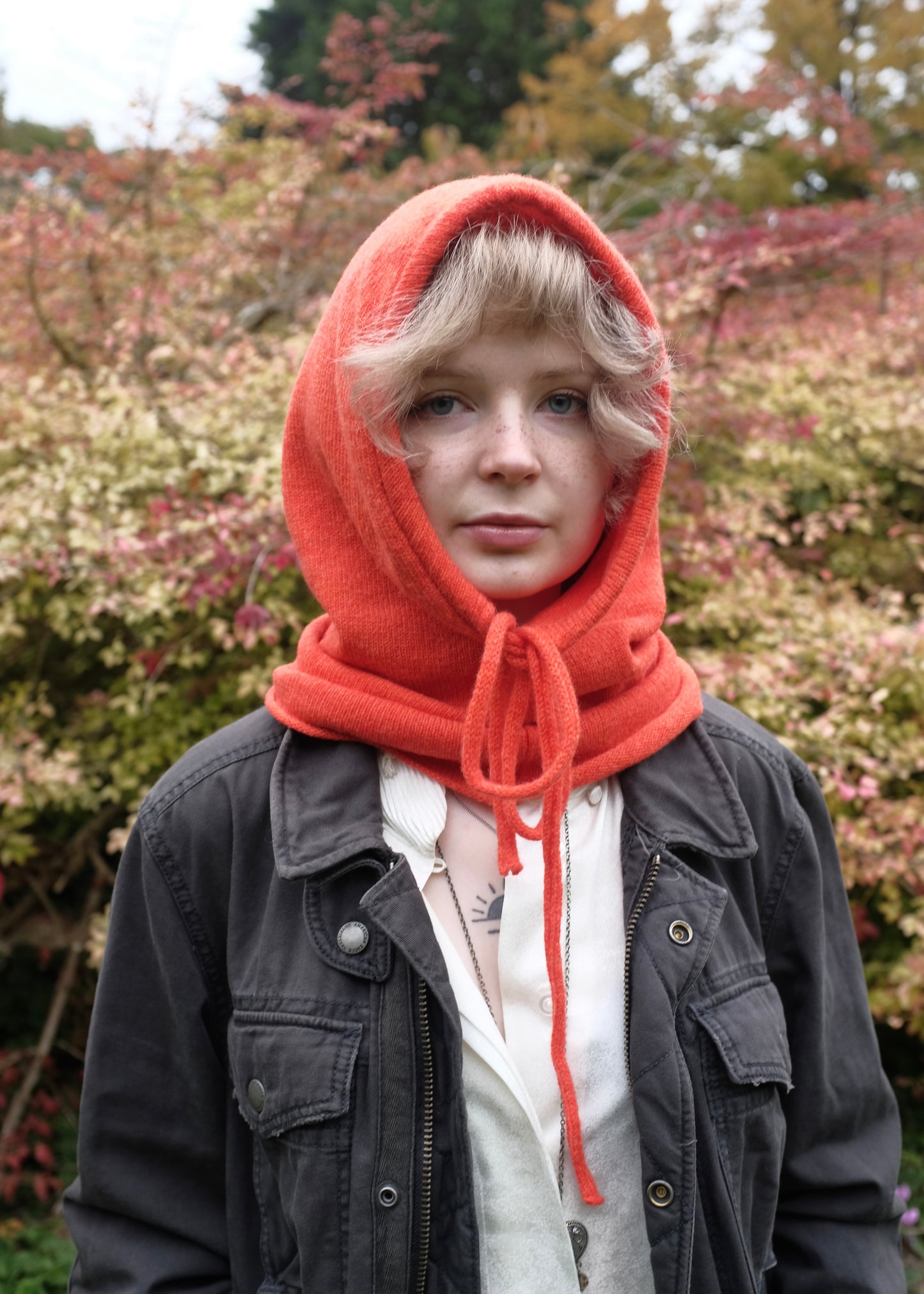 A woman wearing our cashmere knitted balaclava hood in orange outoors 