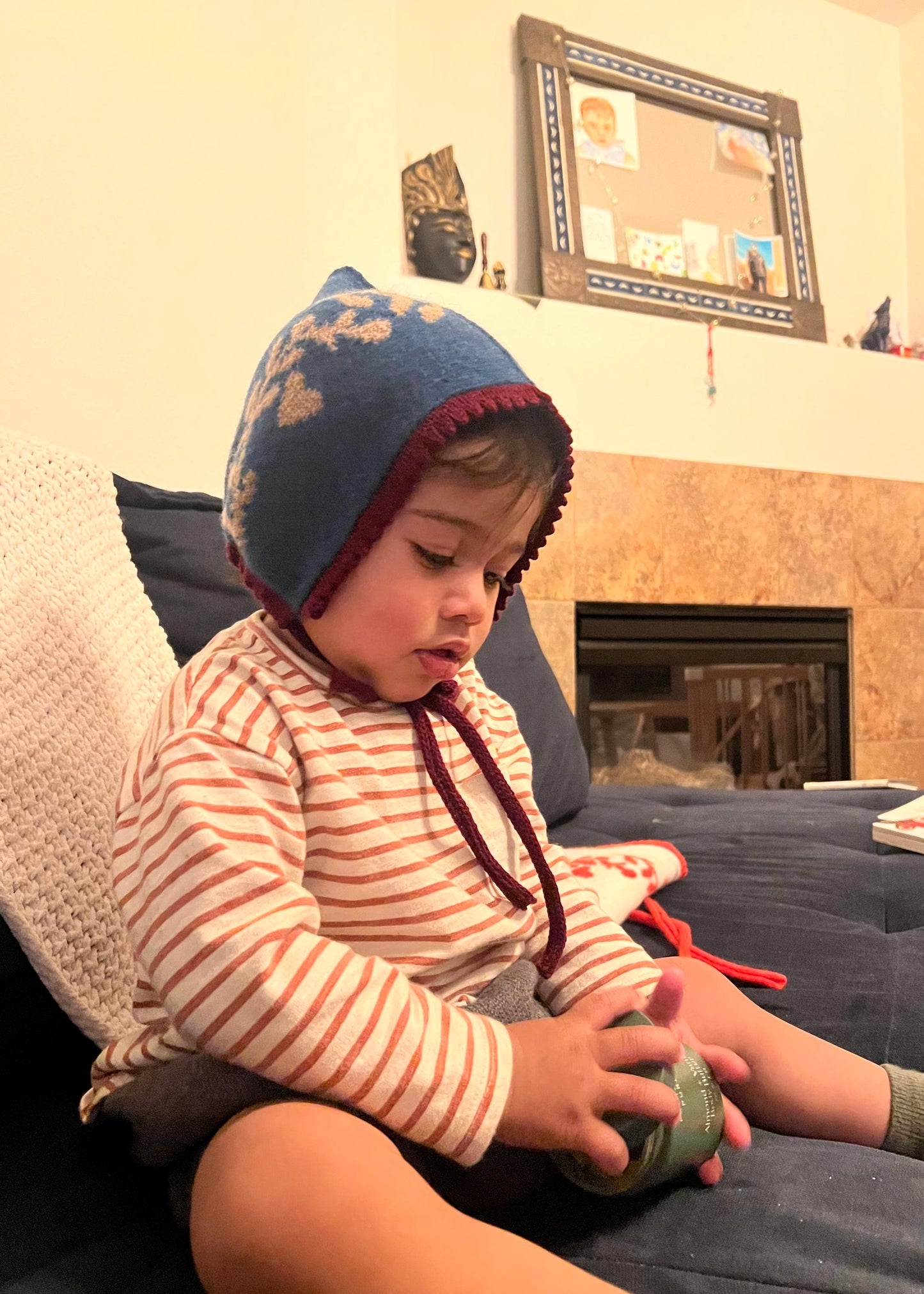 Child wearing a blue bonnet sitting on a couch holding a green toy.