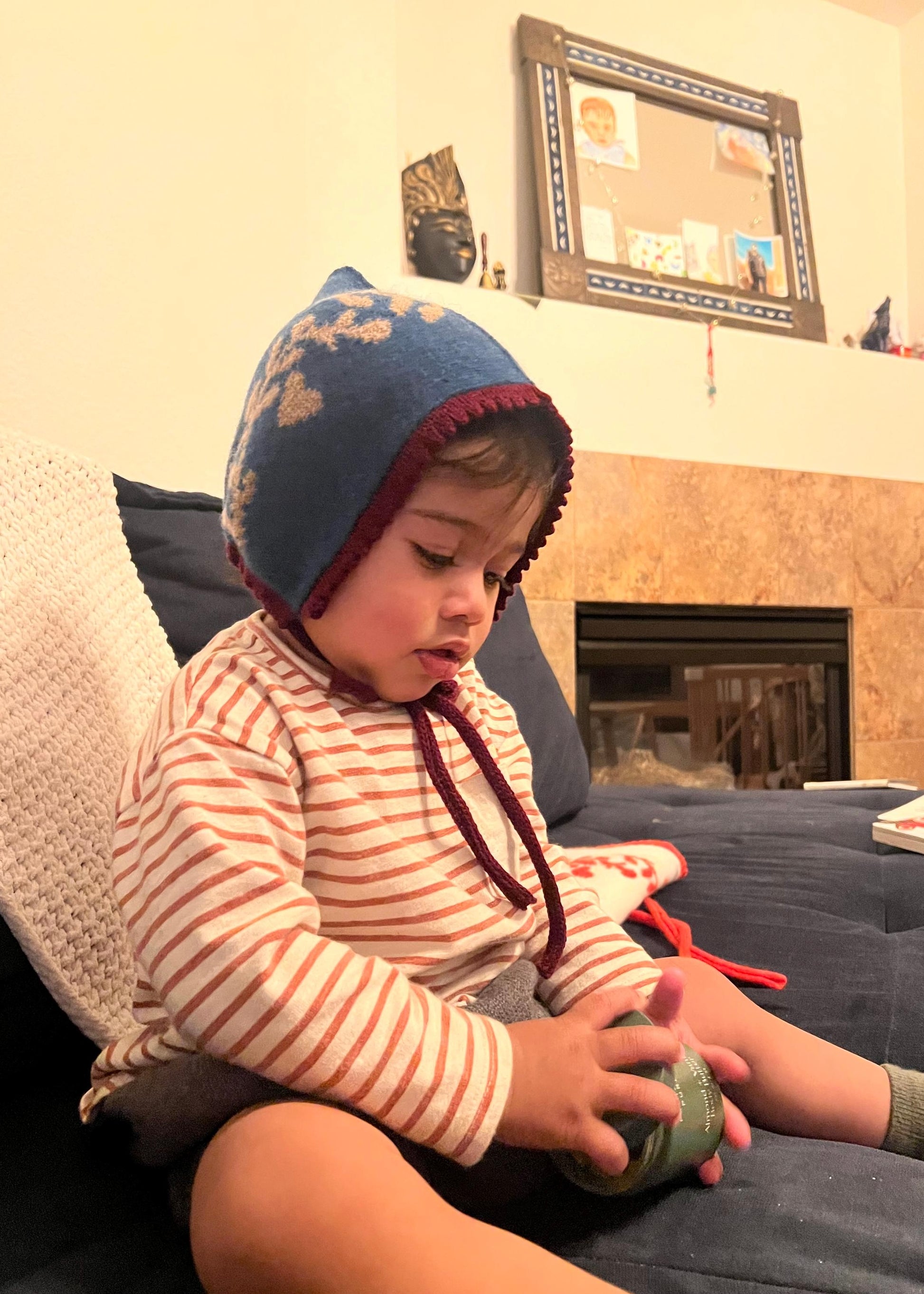 Child wearing a blue bonnet sitting on a couch holding a green toy.