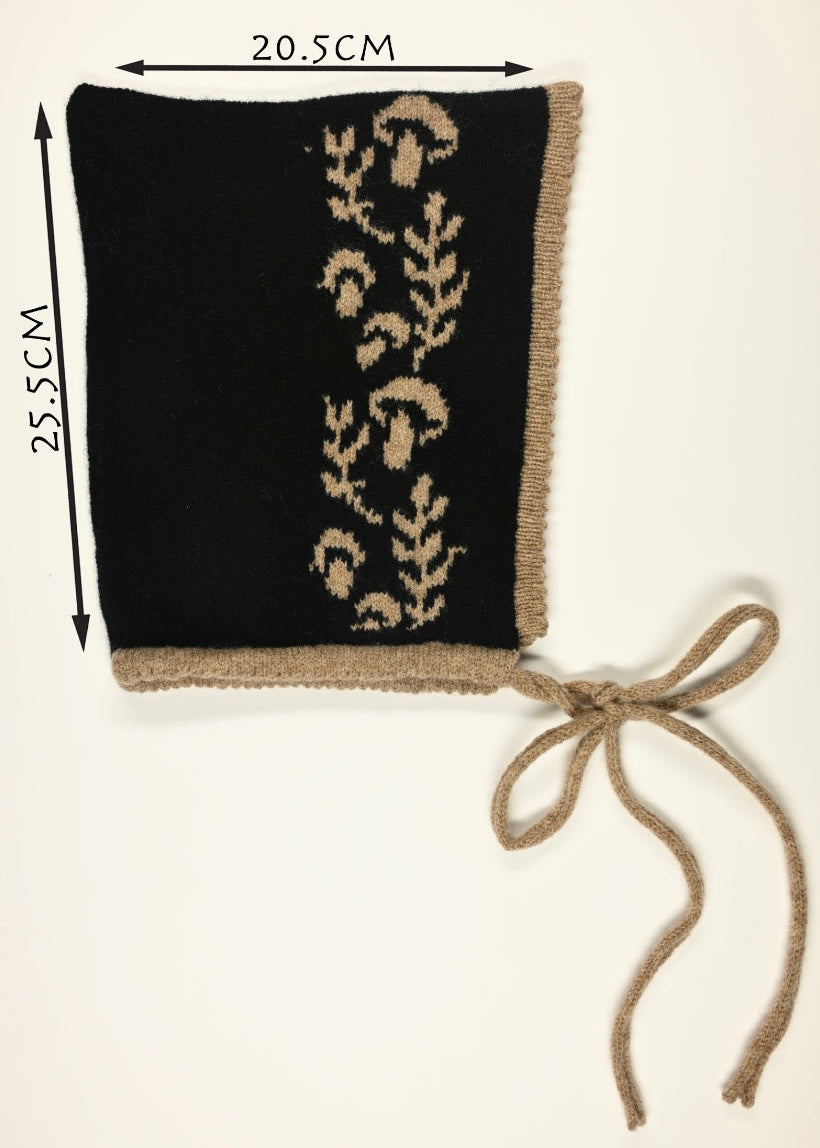 Black knitted bonnet with beige floral mushroom pattern and measurements (20.5cm wide by 25.5cm long) a white background