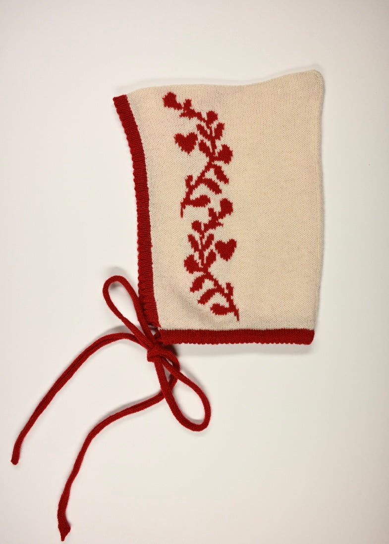Knitted bonnet with red floral laurel leaf pattern on a white background