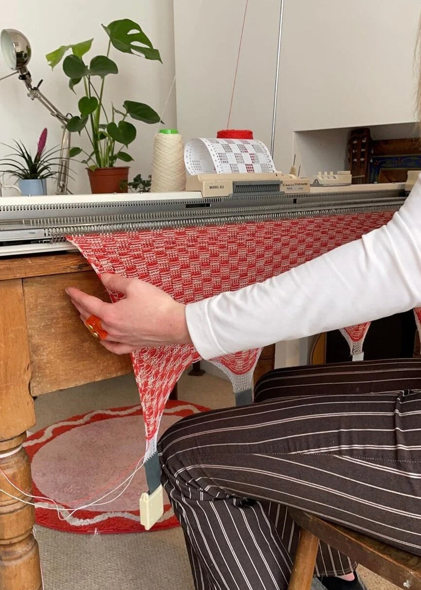 Person using a knitting machine with a red and white patterned fabric.