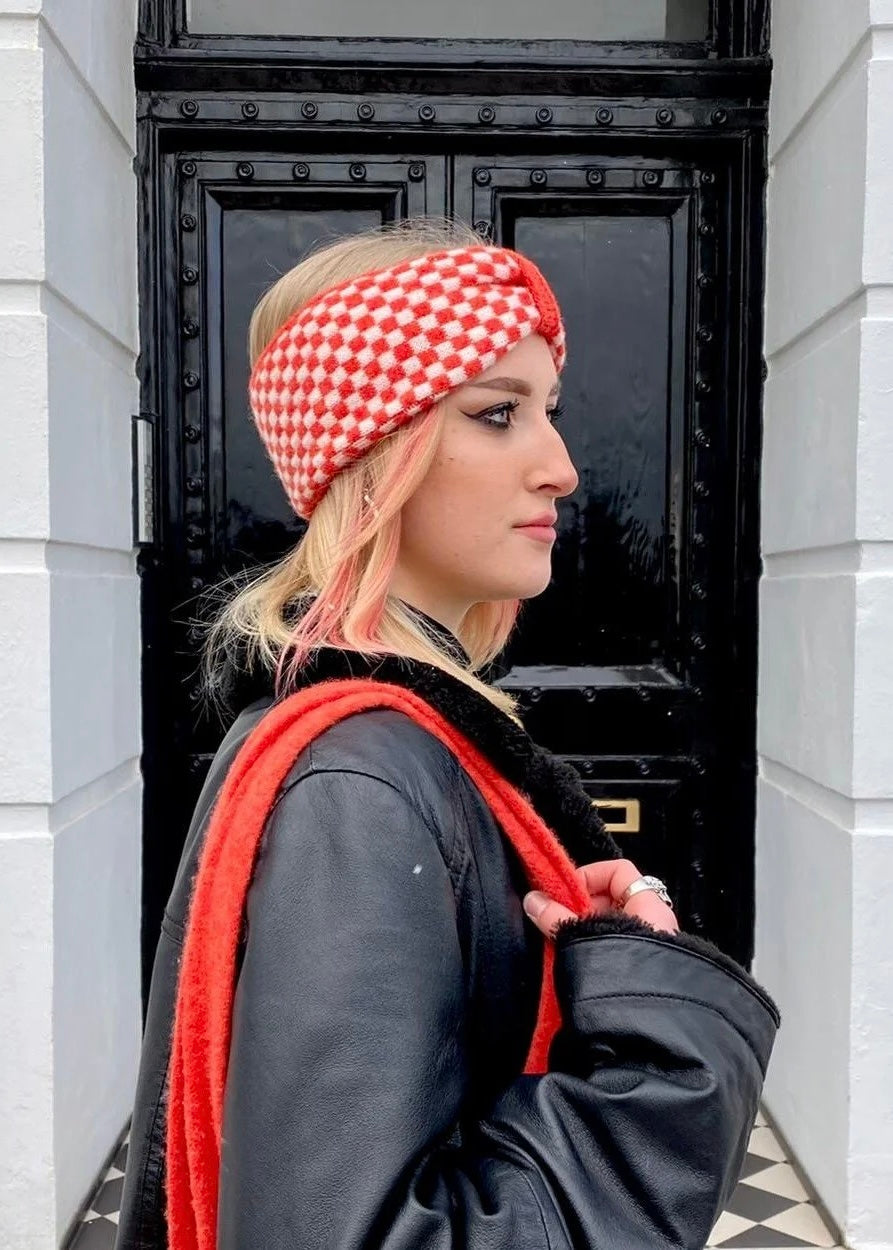 Woman wearing a red and white checkered knitted headband in front of a black door.