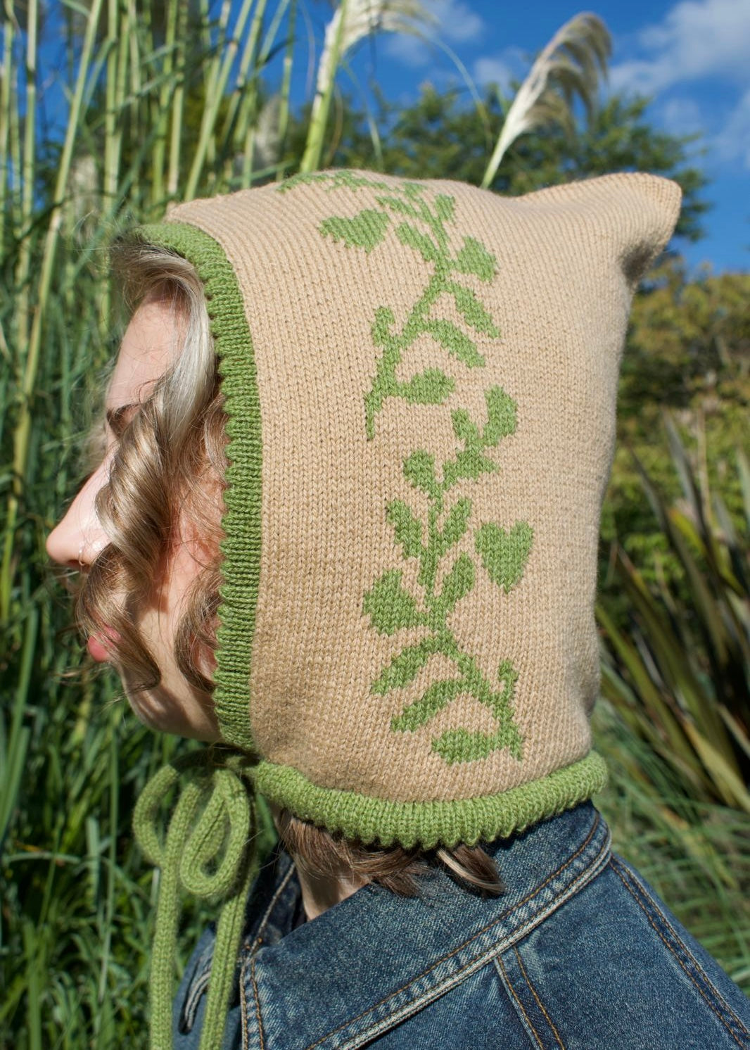 Person wearing a knitted bonnet with green pattern in a natural setting