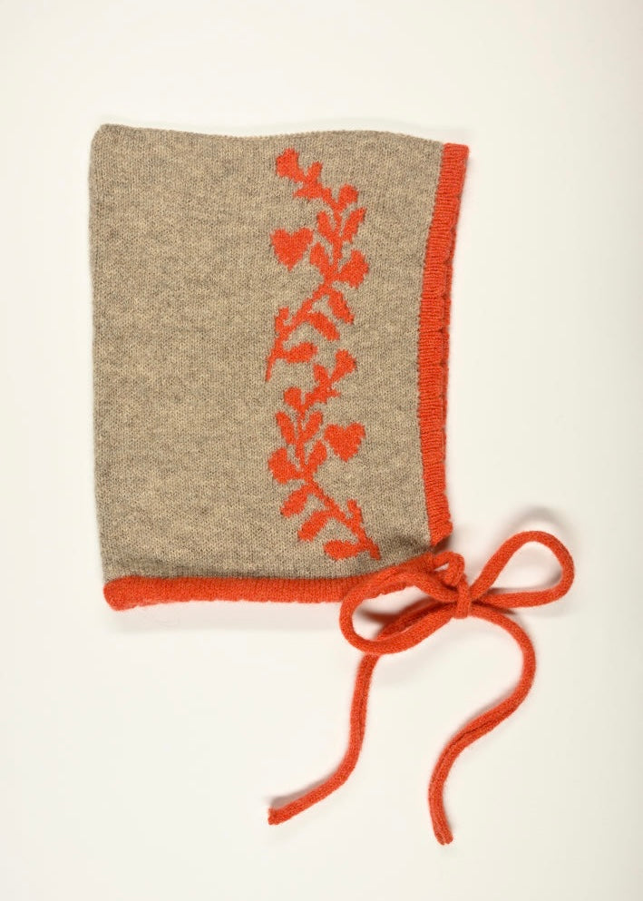 Tan knitted bonnet  with an orange design of laurel leafs and drawstring on a white background