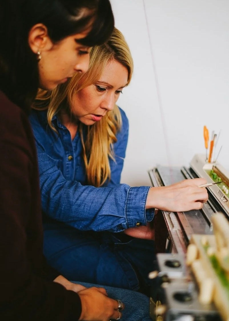 Two women looking at a knit machine together in an indoor setting