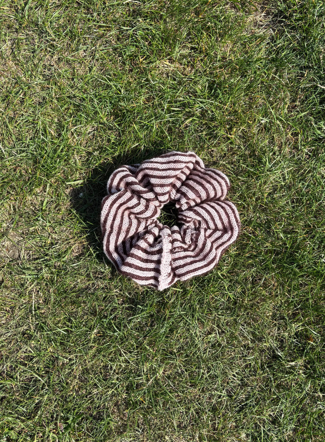 A striped cashmere and mohair knitted oversized scrunchies lying on grass coloured plum and pink 