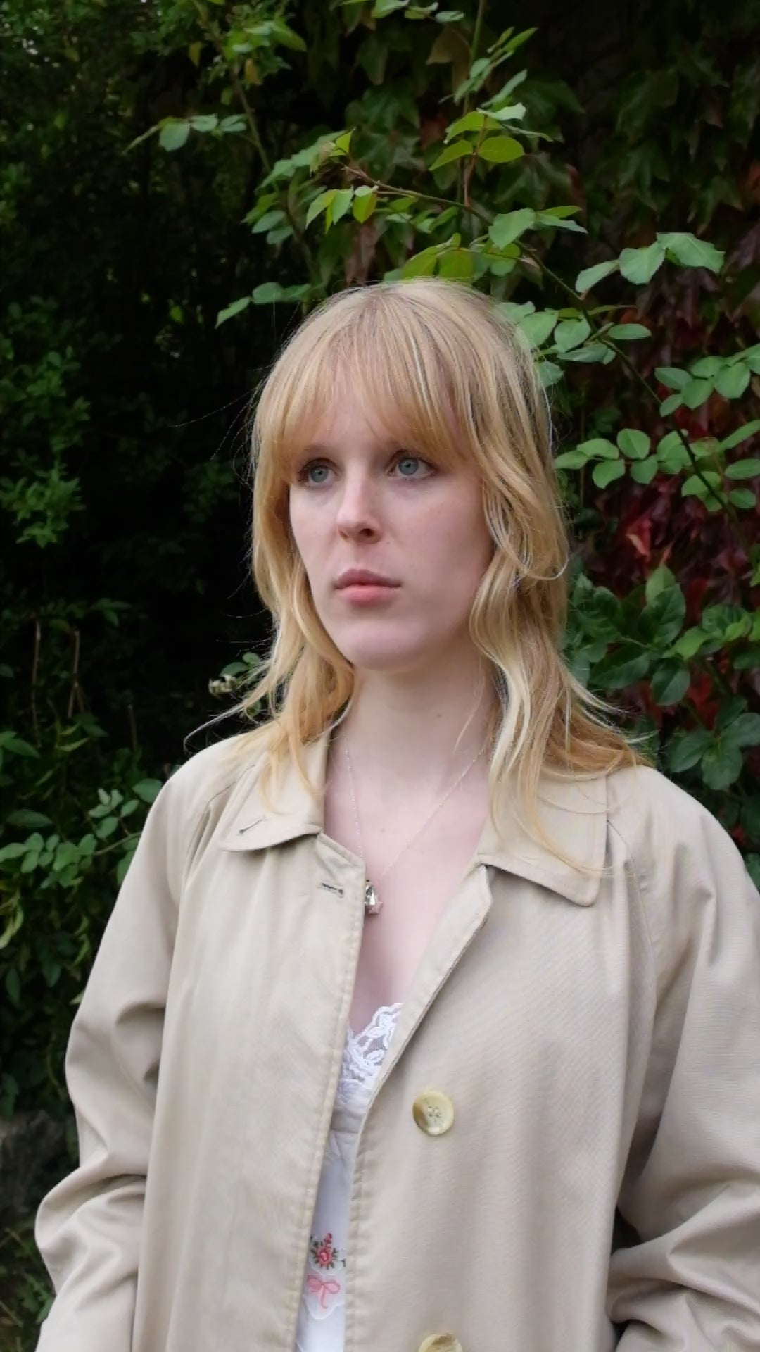 A video of a women wearing a lambswool hand crafted bonnet, with a scarf detailing around the bottom. The main colour of the bonnet is navy. With a white trim, and around the scarf detailing there is a celestial print of the moon and stars in white with gold shimmering details. Behind the women is a blurry mix of green and red leaves 